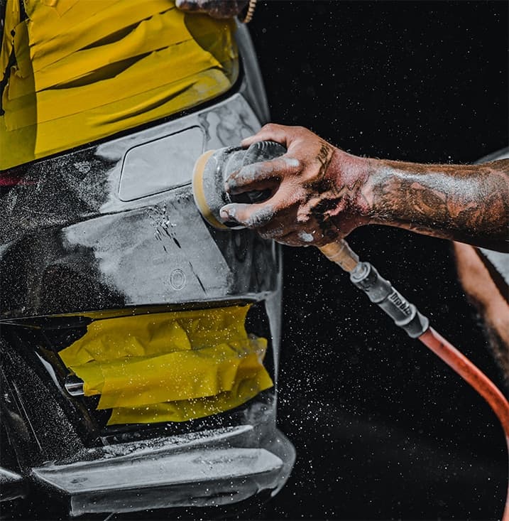A technician sanding a scuffed bumper during cosmetic reconditioning